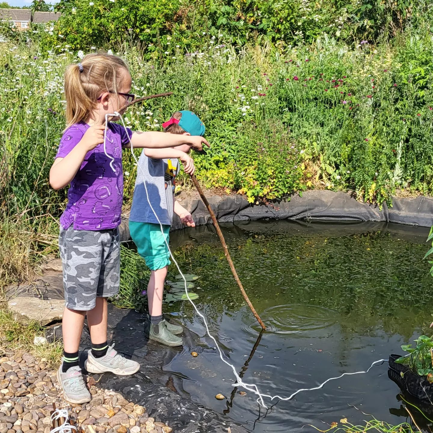 A young boy and girl playing by the side of a pond