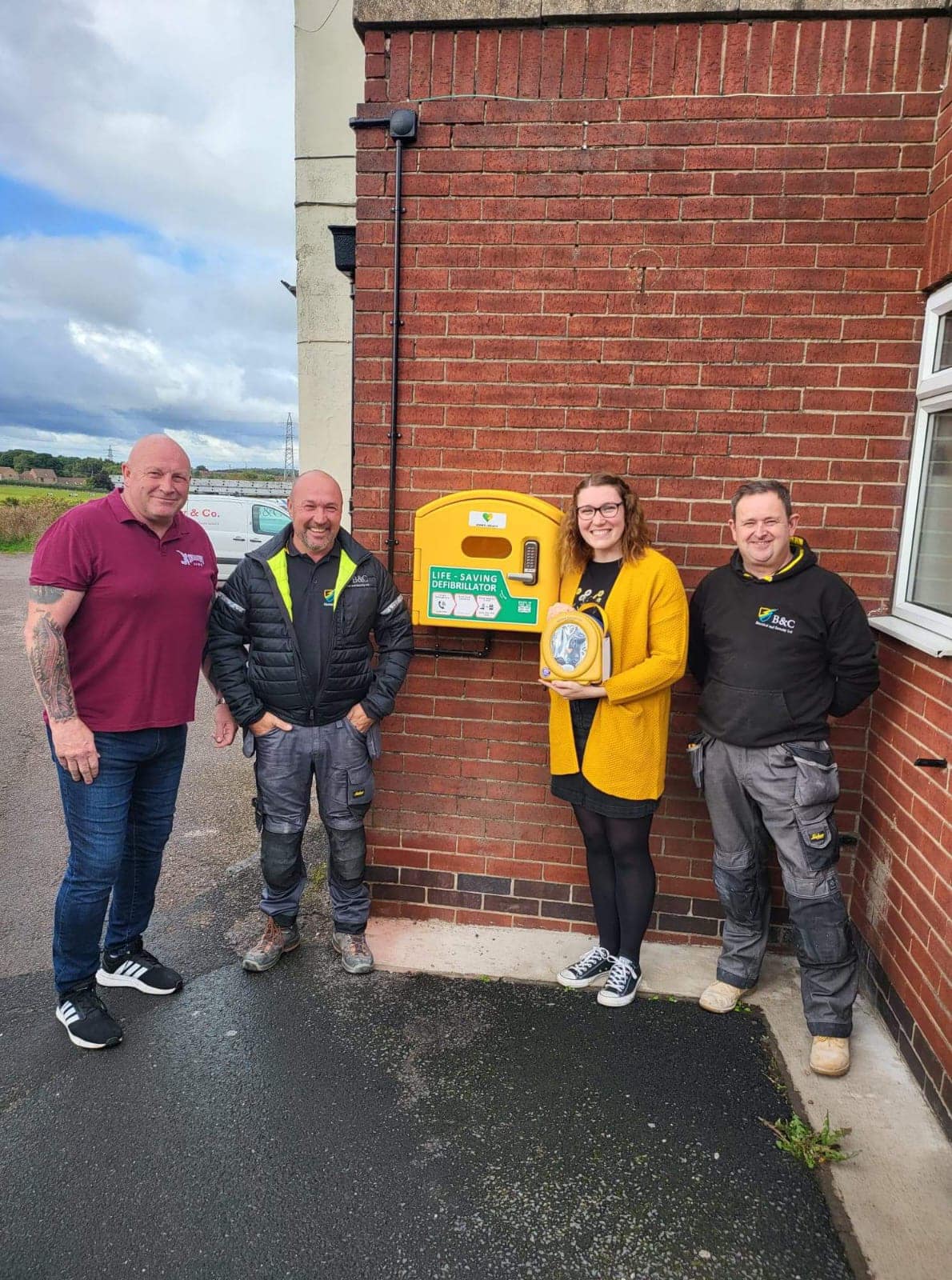 Holly Younger and three men next to a defibrillator installation