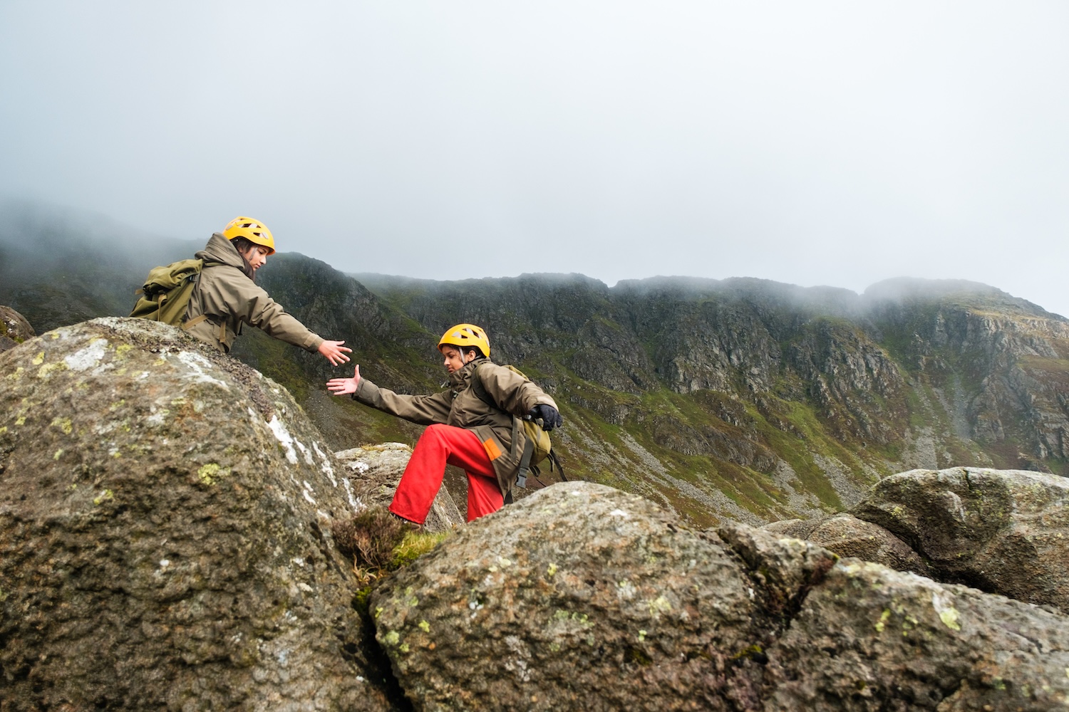 Two young people clambering across some rocks